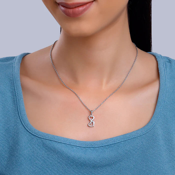 Person wearing a silver necklace with a heart pendant on a plain background